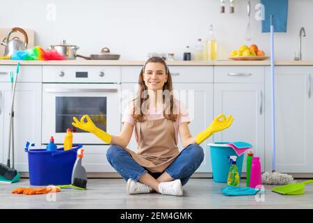 Happy Millennial Hausfrau sitzt in Lotus Yoga Pose auf Küche Boden umgeben von Reinigungsmitteln Stockfoto