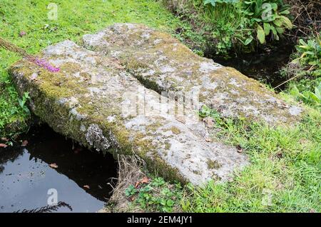 Eine einfache Natursteinfußbrücke, die einen kleinen Bach überquert Ein englischer Garten Großbritannien Stockfoto