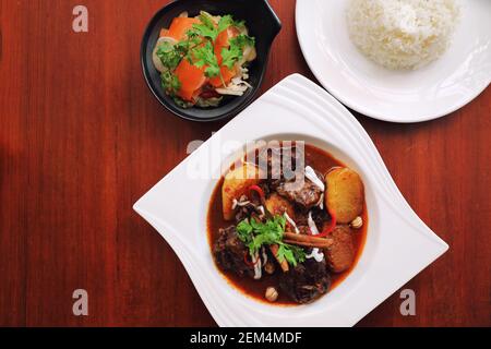 Rindfleisch Massaman Curry mit Reis und Salat auf Holz- Hintergrund, Thai Food Stockfoto