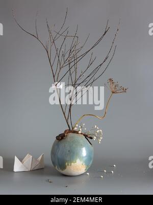 Komposition mit getrockneten Pflanzen in einer runden Keramikvase und Papierbooten. Stockfoto