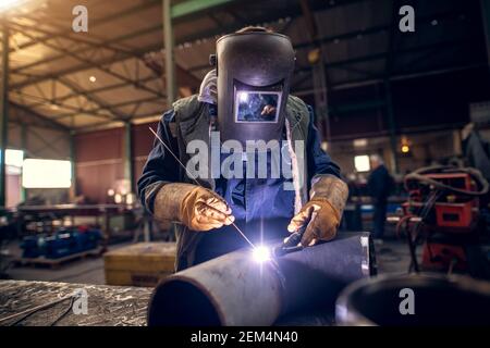 Nahaufnahme Porträt Ansicht von professionellen Maske geschützt Schweißer Mann In Uniform arbeiten an der Metallskulptur am Tisch In der industriellen Stofffabrik Stockfoto