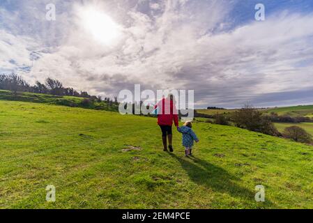 Coombe Bissett Down, Coombe Bissett, Salisbury, Wiltshire, Großbritannien, 24th. Februar 2021: Frau, die bei frühlingshaften Wetter mit Kleinkind in der offenen Landschaft des Naturreservats Kreide Downland spazierengeht. Die Temperaturen stiegen bis in die Mitte der Teenager, so dass es ein ungewöhnlich milder Tag. Kredit: Paul Biggins/Alamy Live Nachrichten Stockfoto