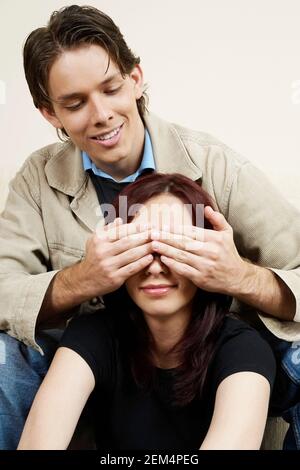 Nahaufnahme eines jungen Mannes, der die Augen einer jungen Frau bedeckt Augen von hinten Stockfoto