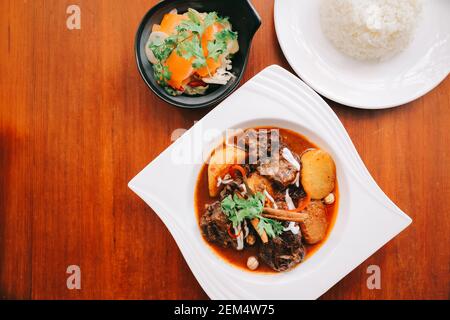 Rindfleisch Massaman Curry mit Reis und Salat auf Holz- Hintergrund, Thai Food Stockfoto