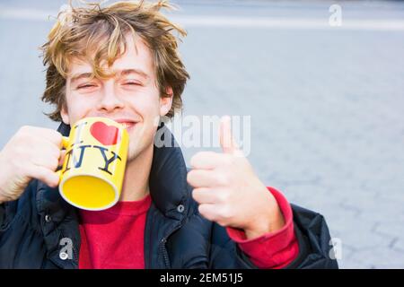Porträt eines jungen Mannes mit einer Kaffeetasse und Zeigt ein Daumen nach oben Stockfoto