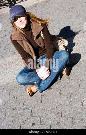 Porträt einer jungen Frau, die mit auf der Straße sitzt Ihre Beine kreuzten sich Stockfoto