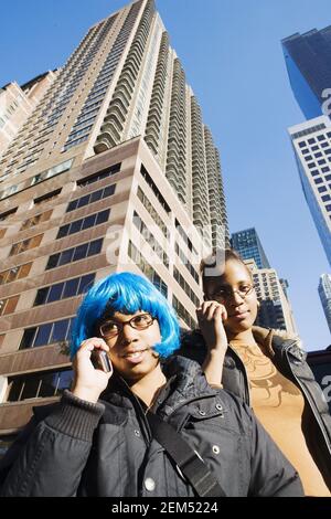 Low-Angle-Ansicht von zwei jungen Frauen sprechen auf Mobiltelefonen, New York City, New York State, USA Stockfoto