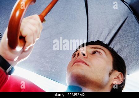 Low-Angle-Ansicht eines jungen Mannes, der einen Regenschirm hält Stockfoto