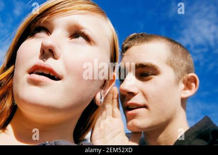 Nahaufnahme eines jungen Mannes, der in die einer jungen Frau flüstert Ohr Stockfoto