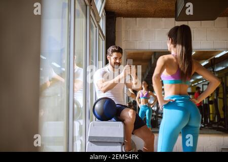 Attraktive gut aussehende bärtige muskulösen Mann sitzt in der Ecke der Die Turnhalle auf Steppern und machen ein Foto mit Handy Von seiner Form sportliche Fitness mädchenf Stockfoto