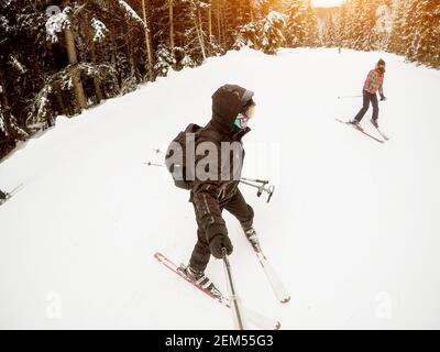 Mann im Skianzug erfassen einen schönen Moment mit einem attraktiven Mädchen im Hintergrund im Wald beim Skifahren. Stockfoto