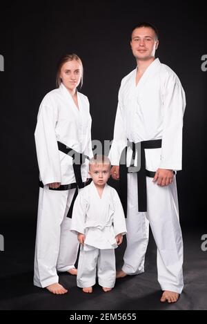 Porträt einer glücklichen jungen Familie in Kampfkunstuniform, die auf schwarzem Hintergrund steht. Stockfoto