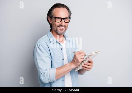 Portrait von gut aussehend clever fröhlich reifen Mann schriftlich Notizen Planung Tag isoliert auf grauem pastellfarbenem Hintergrund Stockfoto