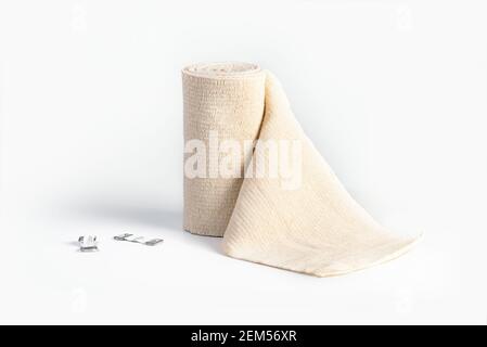 Gewebter elastischer medizinischer Verband, der in Rollen- und Fixierclips gerollt wird. Kompressionsbandage auf weißem Hintergrund Stockfoto