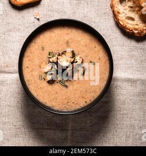 Pilzsahnesuppe serviert mit geröstetem Brot auf Leinen, Blick von oben Stockfoto