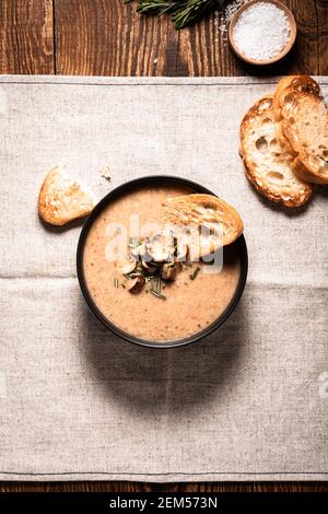 Pilzsahnesuppe serviert mit geröstetem Brot auf Leinen auf rustikalem Holztisch, Blick von oben Stockfoto