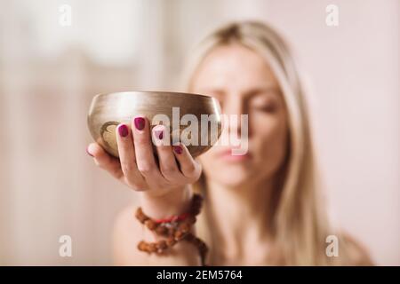 Blonde Frau, die Yoga praktiziert, hört die Melodie aus der tibetischen Schale, Nahaufnahme Stockfoto