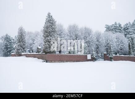 Schöne Winterlandschaft mit Blick auf verschneiten Friedhof in Travnik Dorf umgeben von roten Backsteinmauer, schneebedeckten Feldern und Frost Baum auf bewölkt Stockfoto