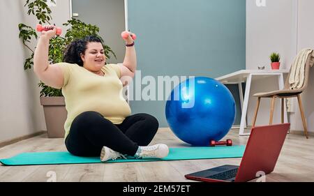 Übergewicht Frau macht Übungen zu Hause mit Online-Personal Trainer Für die Gewichtsabnahme mit Kurzhanteln Stockfoto