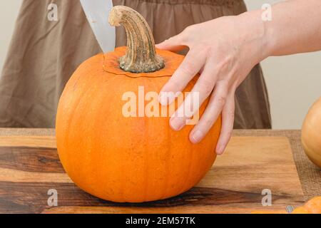 Frau schneidet reifen orangefarbenen Kürbis auf Holzbrett. Schritt für Schritt Kürbispüree Rezept, Lifestyle Stockfoto