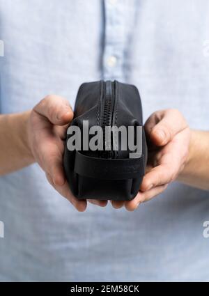 Herren-Kosmetiktasche aus schwarzem Leder oder Tasche für Toilettenartikel in Herrenhänden in blauem Hemd. Stil, Retro, Mode, Vintage und Eleganz. Stockfoto