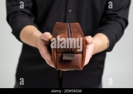 Herren braune Leder persönliche Kosmetiktasche oder Tasche für Toilettenartikel-Zubehör in einem Herrenhände in schwarzem Hemd. Stil, Retro, Mode, Vintage und Eleganz Stockfoto