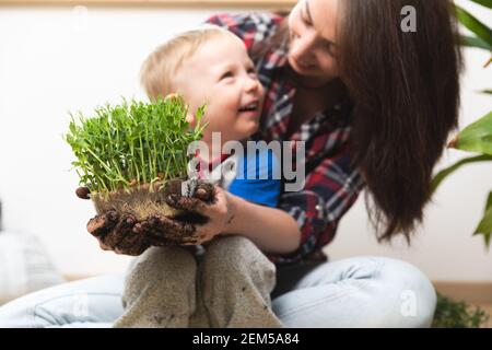 Hobbys zu Hause Gartenarbeit - Junge Mutter und Kind hält Erbsen mit Sprossen in Behälter mit sichtbaren Wurzeln in Händen mit Schmutz bedeckt und lächelnd. Stockfoto