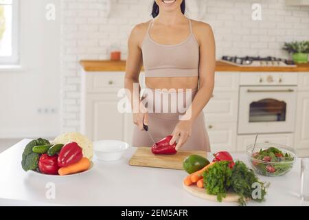 Ein kurzer Schuss glücklicher Frau, die Paprika hackt, während sie gesund macht Vegetarischer Salat Stockfoto