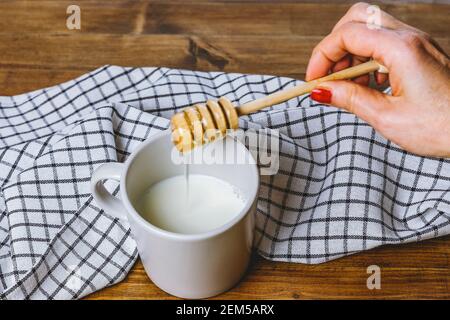 Eine weibliche Hand benutzt einen Honigtauer, um ihn zu gießen In eine Tasse Milch Stockfoto