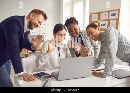 Team von glücklichen, vielfältigen Geschäftsleuten winkt hallo zu ihren Kollegen während eines Videoanrufs Stockfoto