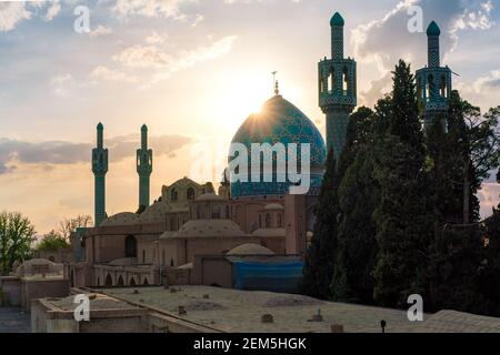 Die Sonne untergeht hinter der blauen Kuppel der Vali Shrine Moschee, die von einem Dach aus betrachtet wird. Auf dem Dach des Schah Nematollah Vali Schreins, Mahan, Iran, Persien. Stockfoto