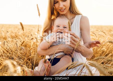 Glückliche schöne Mutter mit ihrem Baby auf dem goldenen Weizenfeld, Familie auf dem Getreidefeld, Mama umarmt ihren kleinen Jungen Stockfoto