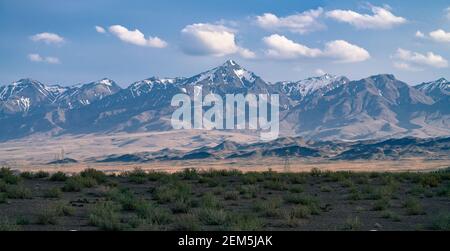 Hohe Berge mit Schnee auf der Spitze ragen über der iranischen Wüste. Majestätische Viertausender in einem weichen Dunst an einem sonnigen Tag im alten Persien, Iran. Stockfoto