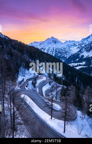 Autos leichte Wege auf den kurvenreichen Kurven der Malojapassstraße im Winter bei Sonnenuntergang, Bregaglia Tal, Kanton Graubünden, Engadin, Schweiz. Stockfoto