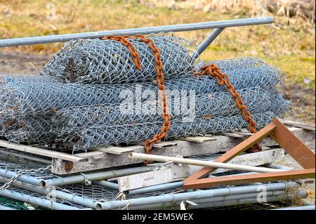 Ein Stapel aufgerollter, weggeworfener Kettengliederzäune mit einer verrosteten Kette. Stockfoto