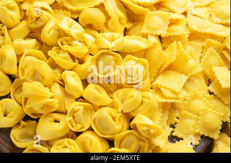 Tartollini mit Käse oder Fleisch zum Kochen in Brühe, verschiedene Formen. Traditionelles Gericht für Feiern in italien, Emilia Romagna Region. Frische hausgemachte Pasta mit Füllung auf einem Holztisch. Stockfoto