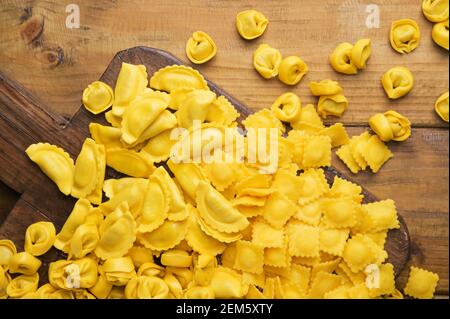 Tartollini mit Käse oder Fleisch zum Kochen in Brühe, verschiedene Formen. Traditionelles Gericht für Feiern in italien, Emilia Romagna Region. Frische hausgemachte Pasta mit Füllung auf einem Holztisch. Oben Stockfoto