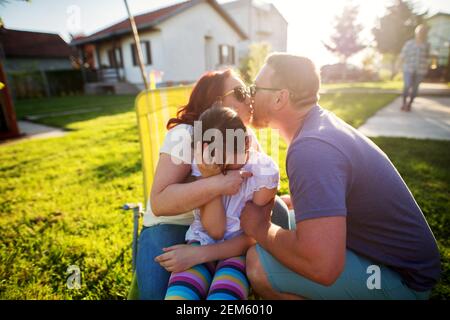 Kleine entzückende Mädchen in bunten Kleidern fühlt sich verlegen und facepalming, weil ihre Eltern öffentlich zeigen Zuneigung durch einen Kuss. Stockfoto