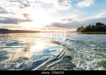 Szenische helle lebendige blau bis rot warmen Sonnenuntergang Abendzeit Landschaft mit Motorboot swirl Spur auf Wasseroberfläche des Sees oder Fluss. Horizont-Küstenlinie Stockfoto