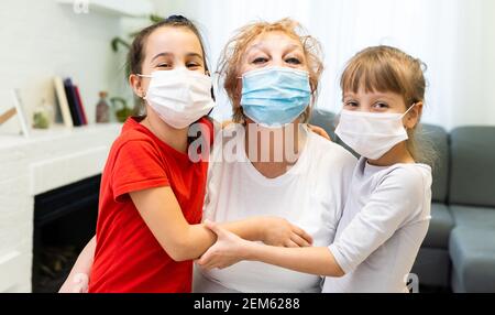 Großmutter und zwei Enkelinnen tragen medizinische Maske. Umarmung, einander trösten Stockfoto