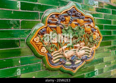 Peking, China - 27. April 2010: Verbotene Stadt. Nahaufnahme von Keramik-Kunstwerken mit Blumen- und Vogelmotiven an der grünen Wand. Stockfoto