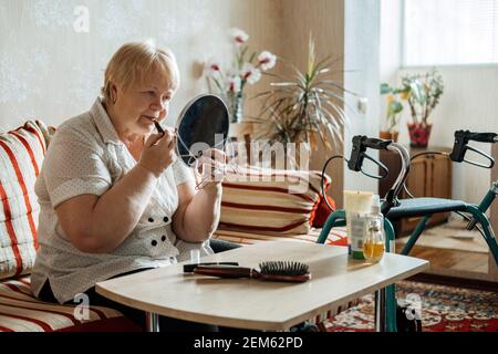 Ältere Schönheit und Hautpflege. Ältere ältere Menschen plus Größe blonde Frau mit Behinderung Anwendung Lippenstift in der Nähe des Spiegels zu Hause. Stockfoto