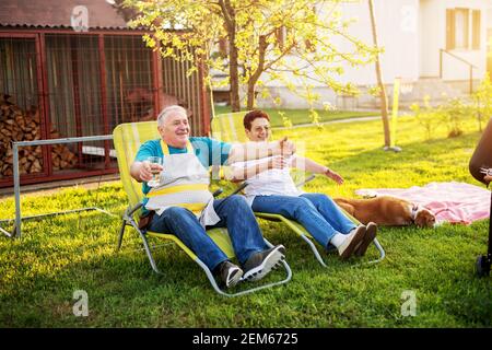 Ältere Paare spreizen ihre Arme und rufen ihr Enkelkind an, vor ihr Haus zu kommen, während der Hund neben ihnen liegt. Stockfoto