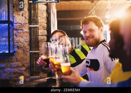 Freundliche Fußballfans sitzen an der Kneipentheke und grüßen sich gegenseitig und wünschen sich gegenseitig viel Glück im kommenden Spiel. Stockfoto