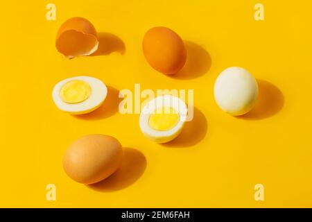 Braunes Huhn roh und hart gekochte frische Eier auf gelbem Hintergrund. Gesundes Essen oder Happy Easter Konzept. Draufsicht, flach liegend Stockfoto