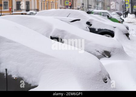 Geparkte Autos mit Schnee bedeckt auf einer unbeschneiten Straße nach Schneefall. Schlechtes Winterwetter. Stockfoto