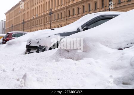 Geparkte Autos mit Schnee bedeckt auf einer unbeschneiten Straße nach Schneefall. Schlechtes Winterwetter Stockfoto