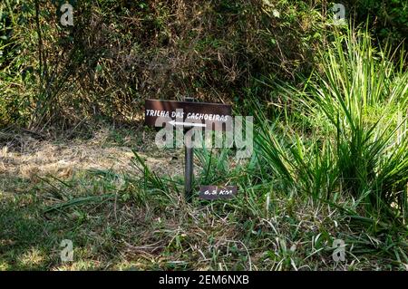 Ein Holzschild in Richtung Trilha das Cachoeiras (Wasserfall-Pfad) Pfad mit einem Wegweiser unten in Serra do Mar Landschaftspark. Stockfoto