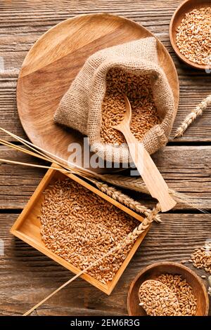 Beutel und Schachtel mit Weizenkörnern auf Holzhintergrund Stockfoto