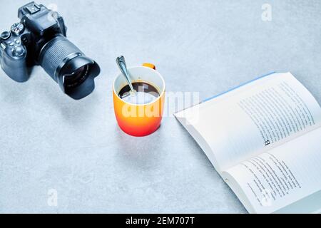 Offenes Buch, Kamera und Kaffeetasse mit Löffel auf grauem Tisch Stockfoto